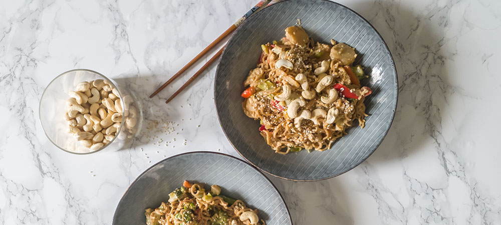 To tallerkener med wok toppet med cashewnødder og sesamfrø